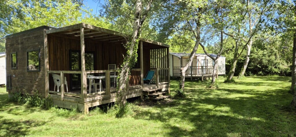 Chalets en bois avec terrasse au milieu des arbres dans un camping verdoyant